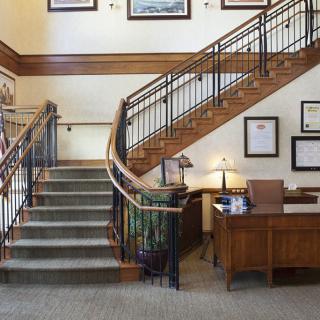 A well-lit office interior with a staircase, wooden desk, and framed artwork on the walls.