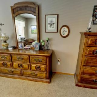 A bedroom with wooden furniture, including a dresser with a mirror and a set of drawers.