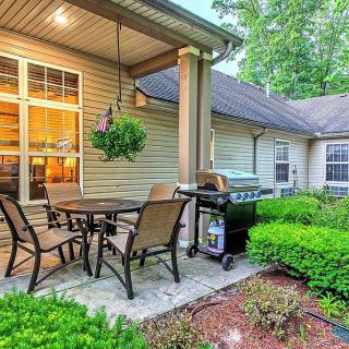 A cozy backyard patio with a dining set and grill, surrounded by lush greenery.