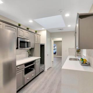 A modern kitchen featuring stainless steel appliances, sleek white countertops, and light wood flooring.