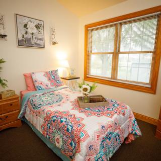 A cozy bedroom with colorful bedding, a wooden nightstand, and a large window.