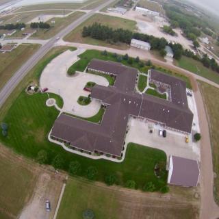 Aerial view of a building complex adjacent to a road, surrounded by greenery.