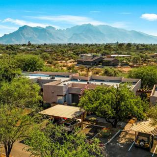 A scenic view of a desert landscape with mountains in the background and a house surrounded by trees.