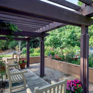 A serene outdoor garden featuring a wooden pergola with seating, surrounded by vibrant flowers.