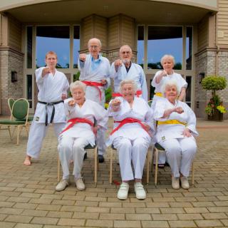 A group of seniors proudly showcase their karate skills in an outdoor setting.