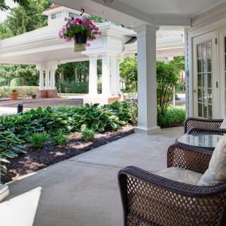 A cozy porch with wicker chairs overlooking a lush garden and patio area.