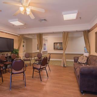 A cozy living room with chairs, a sofa, and a television, featuring warm lighting and wooden flooring.