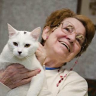 A joyful elderly woman holding a white cat, both sharing a moment of happiness.