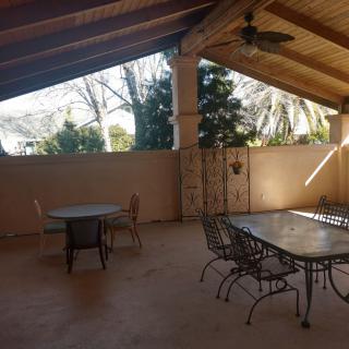 A spacious outdoor patio with a covered roof, featuring tables and chairs, surrounded by trees.