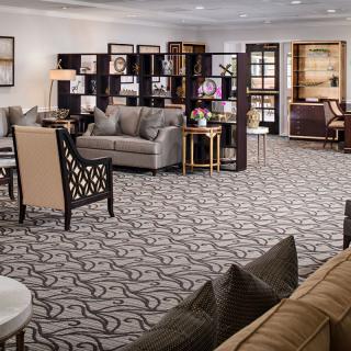 A spacious and elegantly designed living room featuring comfortable seating, a patterned carpet, and decorative shelves.