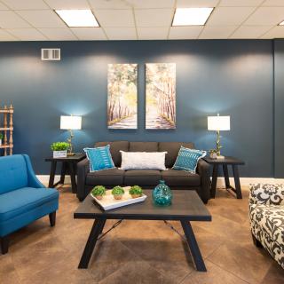 A modern living room with blue walls, featuring a comfortable sofa, armchairs, and decorative elements such as lamps and artwork.