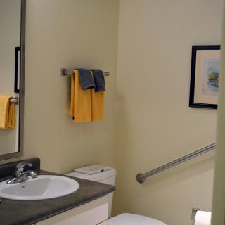 A neatly organized bathroom with a sink, mirror, yellow towels, and a handrail next to the toilet.