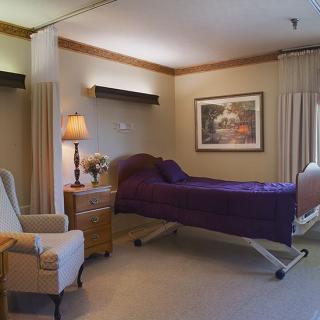 A well-furnished hospital room featuring a bed, comfortable seating, and warm lighting.
