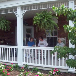 Three people sitting on a porch surrounded by hanging plants and flowers.