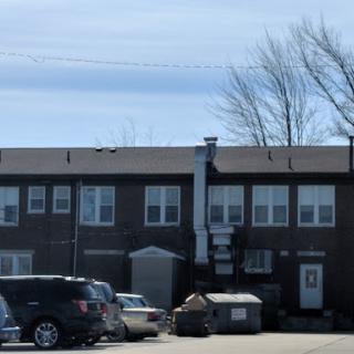 A view of an apartment building with parked cars and a dumpster in the foreground.