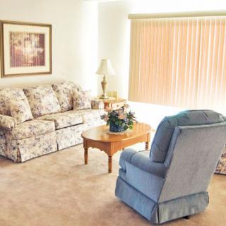 A cozy living room with a floral sofa, blue armchair, and wooden coffee table.