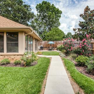 A beautiful backyard with a concrete pathway surrounded by lush greenery and blooming flowers.