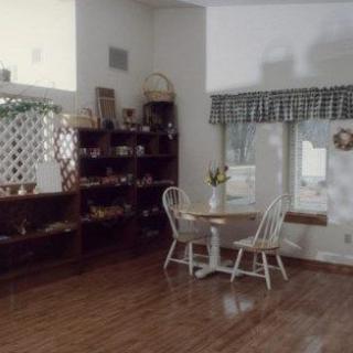 A cozy dining area with a small table and chairs, surrounded by shelves and a large window with checkered curtains.