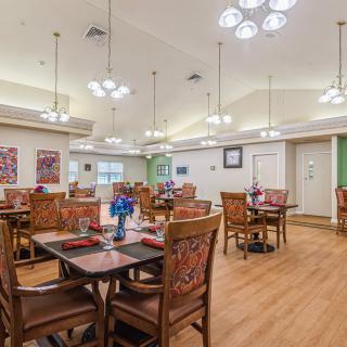 A spacious and elegantly decorated dining room with multiple tables and chairs, featuring modern chandeliers and wooden flooring.