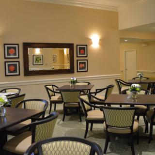A cozy dining area with tables and chairs, decorated with flowers and artwork.