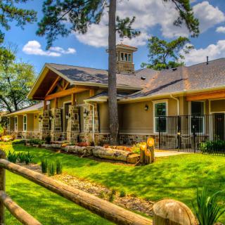 A beautiful house surrounded by a lush garden and tall trees on a sunny day.