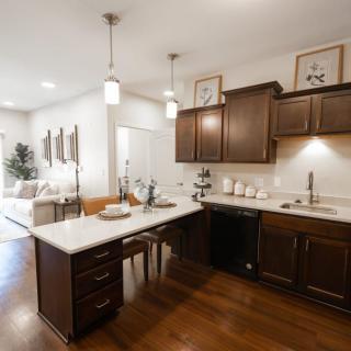 A modern kitchen with dark wood cabinets and a central island, featuring pendant lighting and an open layout.