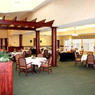 A spacious dining area with elegantly set tables and wooden chairs, featuring large windows and a carpeted floor.