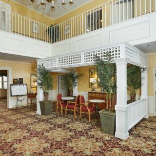 A hotel lobby with decorative plants, seating area, and a balcony overlooking the space.