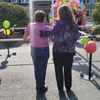 Two people walking towards a colorful balloon display, arm in arm, during an outdoor event.