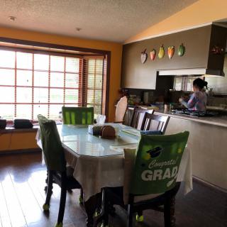 A cozy dining area with a table and chairs, adjacent to the kitchen where someone is preparing food.