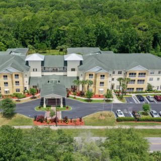 Aerial view of a residential building surrounded by lush greenery with a parking lot in front.