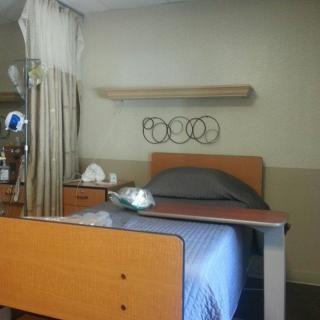 A hospital room with a bed, bedside table, and curtains.