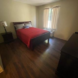 A minimalist bedroom with a neatly made bed, nightstand, and curtains filtering natural light.