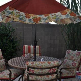 A cozy patio setup with a round table, cushioned chairs, and a floral umbrella.