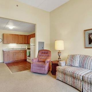 A cozy living room area with a view of the kitchen, featuring a comfortable sofa, recliner chair, and a floor lamp.