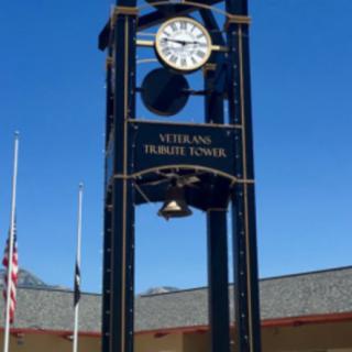 A clock tower at a veterans memorial site with flags in the background.