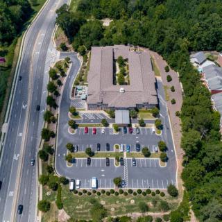Aerial view of an office building surrounded by a parking lot, roads, and trees.