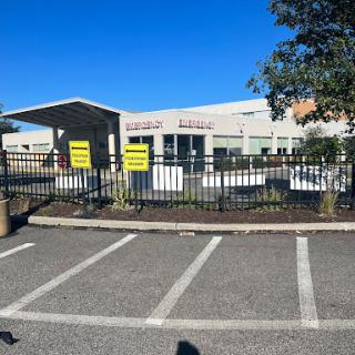 A view of a fenced building with visible signs in a parking lot under a clear blue sky.