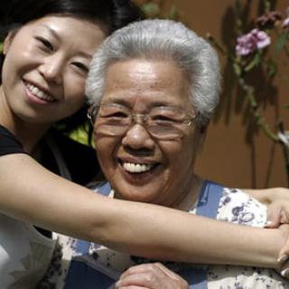 A younger woman smiling and embracing an elderly woman outdoors.