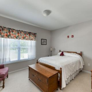 A cozy bedroom with a wooden bed, chest, and a window with floral curtains.