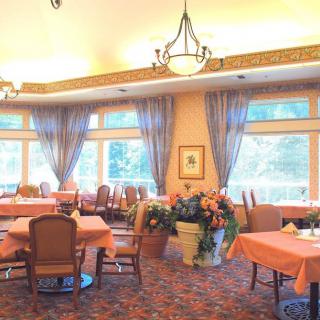 A spacious and elegant dining room with large windows, decorated with flowers, chandeliers, and draped curtains.