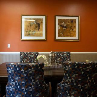 A cozy dining room with patterned chairs and paintings on an orange wall.