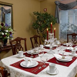 A formal dining room adorned with an elegant table setting, featuring red placemats, white dinnerware, and lit candles.