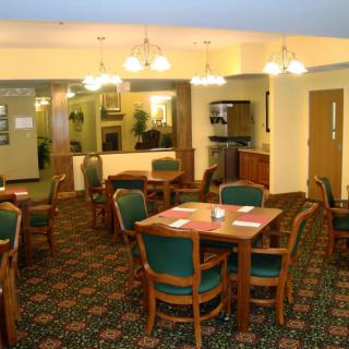 A cozy dining area with wooden tables and chairs, warm lighting, and a patterned carpet.