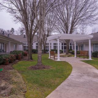 A peaceful courtyard with a winding walkway and a pergola surrounded by trees and benches.