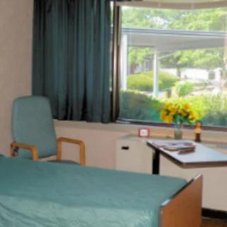 A hospital room interior with a bed, chair, and desk by the window.