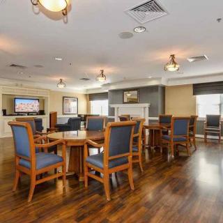 A spacious dining area with wooden floors, multiple tables and chairs, ambient lighting, and a television mounted on the wall.