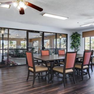 A spacious dining area with a wooden table, cushioned chairs, and large windows overlooking greenery.