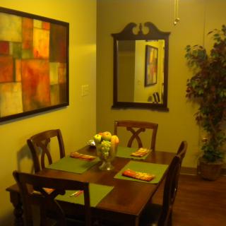 A cozy dining area with a wooden table and chairs, complemented by wall art, a mirror, and decorative plants.