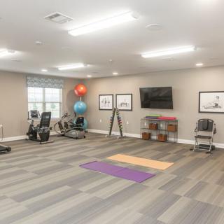 A well-lit exercise room with fitness equipment, including yoga mats, a treadmill, stationary bike, and exercise balls.